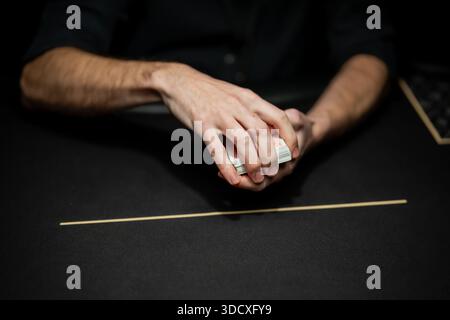 Professioneller Poker-Dealer, der Kartendeck von Hand auf Casino-Tischfilz vorbereitet, konzentriert sich auf sichere Kartenkontrolle während Live-regulierter Glücksspiele Stockfoto