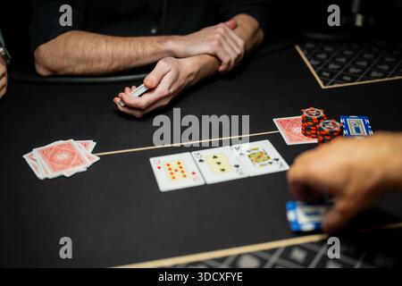 Live-Casino-Poker-Tischszene mit Händlern und Spielern, Community-Karten und gestapelten Chips während regulierter Glücksspiele Stockfoto