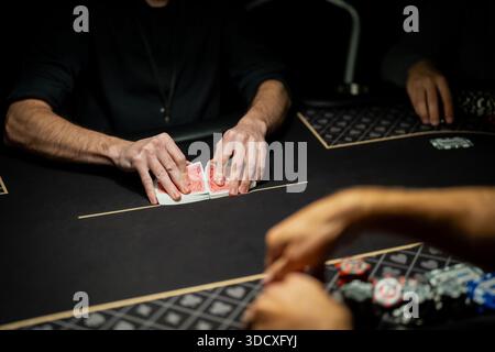 Live-Casino-Poker-Tischszene mit Händlern, die Kartendeck an der Wettlinie trennen, während die Spieler warten und kontrollierte Verfahren der Spielindustrie zeigen Stockfoto