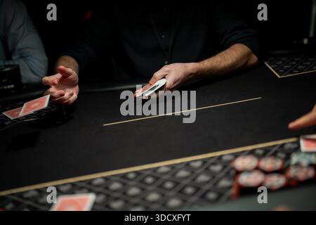 Live-Poker-Table-Action, bei der die Hand des Dealers die Spielkarte über die Filzoberfläche schnippt, während die Spieler warten, und die professionelle Casino-Deal-mec veranschaulicht Stockfoto