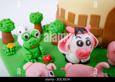 Nahaufnahme von charmanten handgemachten Dekorationen auf einem Kuchen. Nutztiere wie Schweine, Kühe, Frösche, Schafe und Bäume werden aus Fondant-Glasur hergestellt. Stockfoto