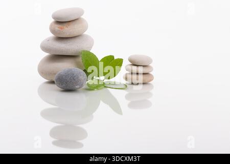 Nahaufnahme von gestapelten Steinen in ausgewogener Form mit frischen grünen Blättern. Konzept für Balance, Meditation, Zen und Spa. Stockfoto