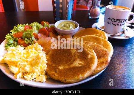 Herzhafte und süße Frühstücksteller mit Rührei, goldenen Pfannkuchen, geräuchertem Lachs, frischen Tomaten und cremiger Avocadosauce Stockfoto