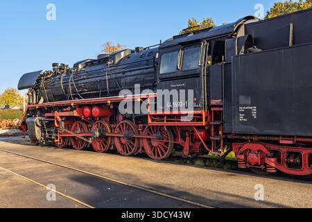 Detaillierte Ansicht der großen roten Antriebsräder und mechanischen Stangen einer schwarzen Vintage-Dampflokomotive, die bei Sonnenlicht auf den Gleisen ruht. Stockfoto