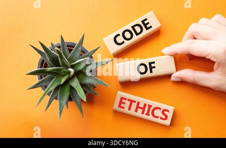 Symbol für Ethikkodex. Konzeptworte Ethik-Kodex auf Holzblöcken. Geschäftsmann Hand. Schöner oranger Hintergrund mit saftiger Pflanze. Business und Stockfoto
