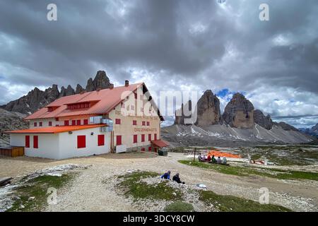 Malerischer Blick auf die Dreizinnenhütte (Rifugio A. Locatelli ? S. Innerkofler), Italien mit Tre Cime di Lavaredo darüber hinaus; Berghütte von 1935 mit roten Rollläden vor bewölktem Himmel Stockfoto