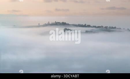 Eine wunderschöne Landschaft, aufgenommen aus Neviano degli Arduini, Italien, zeigt ein ländliches Dorf auf einem Bergrücken, umgeben von dickem, weißem Morgennebel. Stockfoto