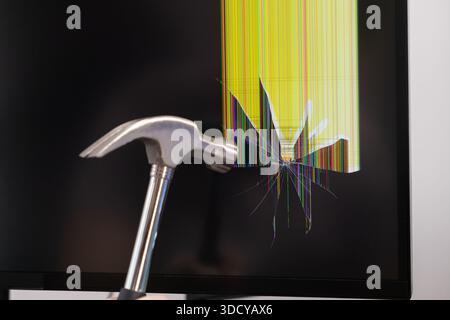 Nahaufnahme eines mächtigen Metallhammers, der auf einen kaputten Computerbildschirm schwingt und farbige vertikal verzerrte Pixel und radiale Risse zeigt. Stockfoto