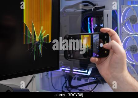 Nahaufnahme einer Hand, die Bilder eines sichtbar beschädigten Computerbildschirms aufnimmt, der helle vertikale Linienartefakte für Versicherungen oder Dienstleistungen in einem Moder zeigt Stockfoto