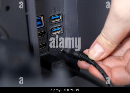 Nahaufnahme einer Hand, die ein Netzkabel an den DC-IN-Anschluss auf der Rückseite eines Geräts anschließt, mit USB- und HDMI-Anschlüssen für vielseitige elektronische Konnektivität Stockfoto
