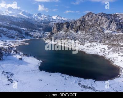 Aus der Vogelperspektive auf den Gletschersee Ercina, seine schneebedeckte Küste und ein hohes felsiges Bergmassiv an einem sonnigen Wintertag. Covadonga, Asturien, Spanien. Stockfoto