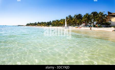 Wunderschöner Strand mit klarem blauem Wasser und Palmen. Der Strand ist voll mit Menschen, die die Sonne und das Wasser genießen Stockfoto