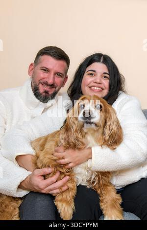 Ein lächelndes Paar hält seinen Hund, während er drinnen zusammen sitzt. Stockfoto