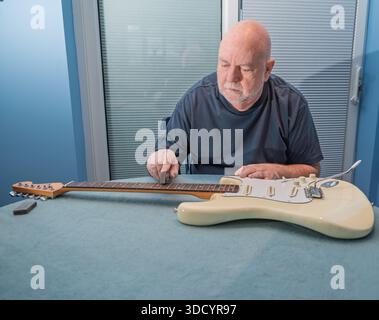 Ein Mann arbeitet an einer Gitarre, vielleicht reinigt oder poliert er die Bünde. Stockfoto