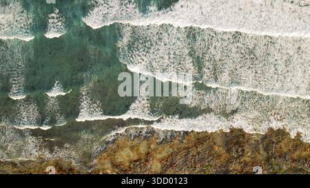 Blick von oben auf das Riff unter den flachen Meereswellen am felsigen Strand. Stockfoto