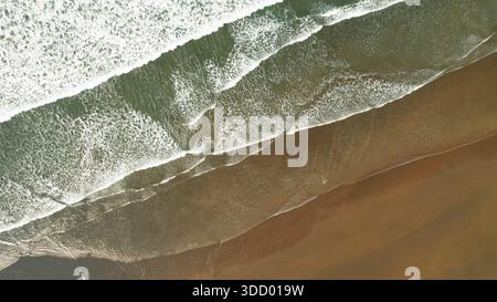Schäumende Ozeanwellen, die den tropischen Sandstrand von oben waschen. Stockfoto