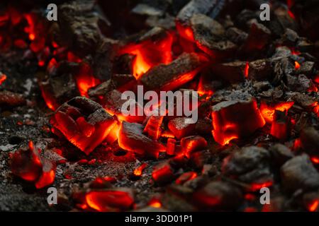 Aktiv schwelende Feuerglut. Hintergrund brennender heißer Kohlen. Flackern brennender Kohlen in der Nacht Stockfoto