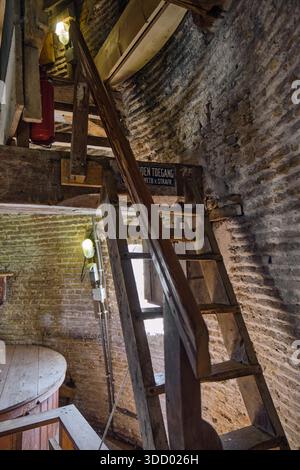 Dieses Stockfoto zeigt das Innere der Rockanje Windmühle in den Niederlanden mit Holztreppen Ziegelwänden und einem Feuerlöscher Stockfoto