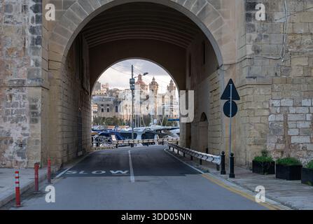 Blick durch einen monumentalen Tunnelbogen, der den Hafen von Birgu umrahmt, mit Booten und historischen Gebäuden, die die maltesische Architektur und mari einfangen Stockfoto
