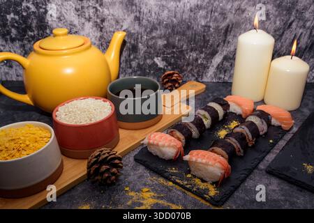 Japanisches Teeset mit Reisschalen und Sushi auf einer Schieferplatte, gemütliches Restaurant Stillleben mit Kerzen und orientalischem Geschirr. Stockfoto