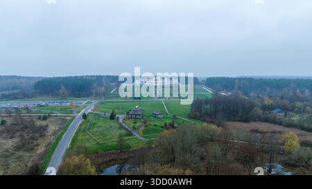 Aus der Vogelperspektive des Ruschany-Palastes in Weißrussland zeigt eine weiße neoklassizistische Fassade, einen zentralen Turm, Flügel, axiale Wege, Treppen, Rasengitter, Autos und Dorf Stockfoto
