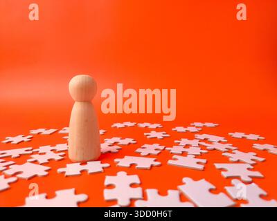 Puppe aus Holz, umgeben von weißen Puzzleteilen auf orangem Hintergrund. Stockfoto