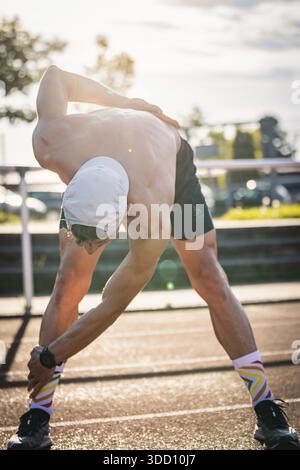 Mann dehnt sich intensiv in sportlicher Kleidung bei Sonnenlicht auf einer Laufstrecke, Triathlon, Calw, Deutschland Stockfoto