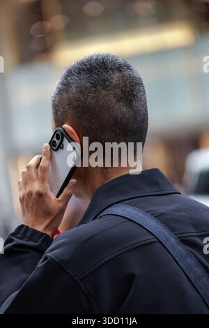 Mann von hinten gesehen, der das Smartphone am Ohr hält. Kurzes graues Haar und eine lässige Jacke verleihen der dynamischen Kommunikation im urbanen Ambiente alltagstauglich. Stockfoto