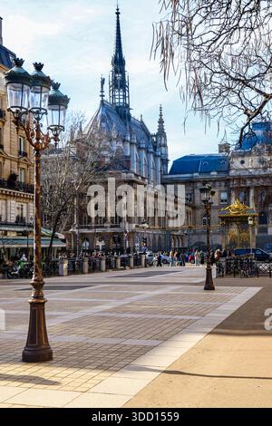 Paris. Der gotische Turm von Sainte-Chapelle erhebt sich über dem historischen Justizpalast in Paris, eingerahmt von kunstvollen Straßenlaternen auf einem sonnigen Stadtplatz. Stockfoto