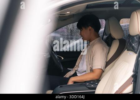 Junger asiatischer Mann lächelt, während er in einem eleganten Innenraum sitzt Stockfoto