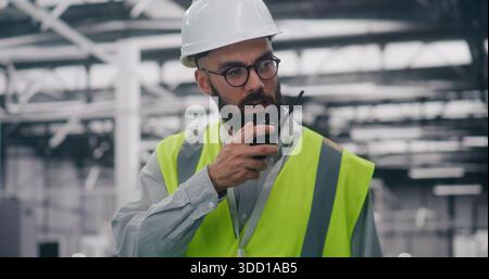 Industrial Management Engineer Leitet Das Team Mit Radio. Spezialist für persönliche Schutzausrüstung weist das Personal an, das Funkgeräte in großen industriellen Umgebungen verwendet. Management, Leitung, Schwerindustrie. Stockfoto