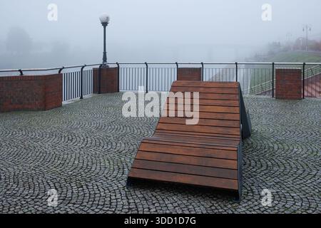 Eine moderne Bank mit A-Rahmen auf einem Stadtboulevard im Nebel. Ein Balkon mit Attika und Bank. Ein Ort zum Entspannen. Stockfoto