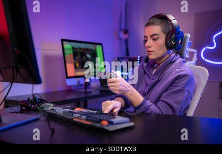 Ein fokussierter Gamer sitzt am Schreibtisch und tippt auf einer mechanischen Tastatur in einem neonbeleuchteten Gaming-Setup. Wenn sie ein Headset um den Hals tragen, sehen sie selbstbewusst aus, während sie sich an einem PC-Gaming oder Streaming-Aktivitäten beteiligen || Modell veröffentlicht Stockfoto
