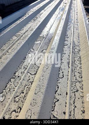 Ein Wellblech liegt flach mit Wassertröpfchen darauf. Das Sonnenlicht reflektiert von der Oberfläche und zeigt die Struktur und das Muster des Metalls. Stockfoto