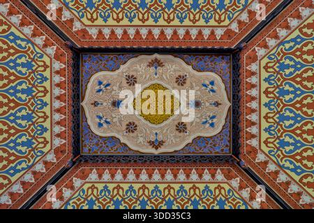 Farbenfrohe, komplexe Holzdeckenkunst mit einem zentralen Medaillon und sich wiederholenden Blumen- und geometrischen Mustern, eingerahmt von dekorativen Bändern. Stockfoto