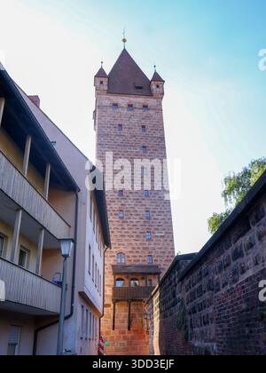 Ein hoher, quadratischer Steinturm in der Nürnberger Altstadt mit roten Ziegeldächern erhebt sich über einer schmalen europäischen Straße mit beigefarbenen Gebäuden. Die Szene Stockfoto