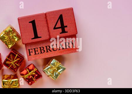 Februar. Komposition zum Valentinstag mit Holzkalender und Geschenkkartons auf rosa Hintergrund. Kopierbereich. Vorstellung eines Tages der Liebe Stockfoto