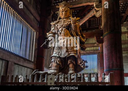 Kōmokuten, eine hölzerne Wächterfigur mit grimmigem Ausdruck und der Namensplatte „廣目“ an ihrem Sockel, steht im Daibutsuden des Tempels Todai-ji in Nara, Japan. Der Bildhauer Unkei begann im frühen 13. Jahrhundert mit der Arbeit an den vier Shitennō (Himmlischen Königen); nur Kōmokuten und Tamonten wurden fertiggestellt. Stockfoto