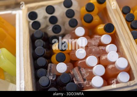 Frischer, kalter Orangensaft und schwarze Kaffeeflasche in Holzkiste mit Eis, das ein erfrischendes Gefühl vermittelt Stockfoto