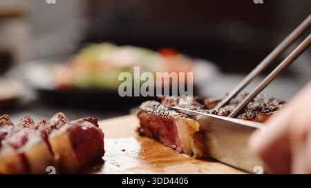 Mann schneidet New york Steak auf Olivenholzbrett Stockfoto