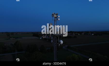 Mobilfunkturm steht vor dem dunkelblauen Himmel, ausgestattet mit verschiedenen Antennen für drahtlose Kommunikation und Mobilfunkdienste im gesamten Po Val Stockfoto
