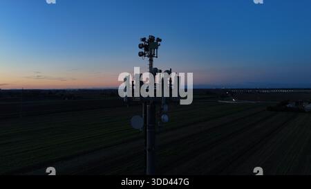 Mobilfunkturm steht vor dem dunkelblauen Himmel, ausgestattet mit verschiedenen Antennen für drahtlose Kommunikation und Mobilfunkdienste im gesamten Po Val Stockfoto