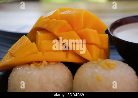 Authentischer thailändischer Mango-Kleberreis, serviert auf einem schwarzen Teller mit Kokosmilch, Reifen Mangoblättern und Kleberreis mit Mungbohnen, wunderschön präsentiert Stockfoto