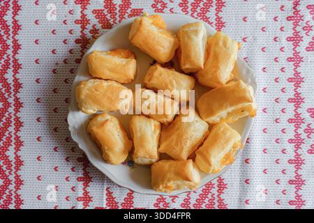 Eine Sammlung goldener herzhafter Gebäckstücke mit Käsefüllung auf einer rustikalen Holzoberfläche. Frisch gebackene Blätterteigbrötchen für kulinarische Zwecke. Stockfoto