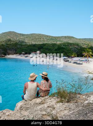 Ein Paar genießt einen ruhigen Moment mit Blick auf den atemberaubenden Grote Knip Beach in Curacao. Das klare türkisfarbene Wasser und der weiße Sand bilden eine perfekte Kulisse für Romantik und Entspannung unter der Sonne. Stockfoto