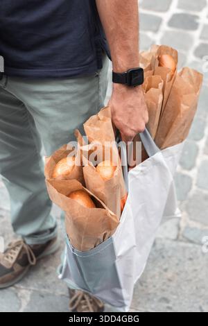 Der Mann hält einen Sack voller Baguettes. Französische Lebensweise, typisches Brot aus der normandie. Essen, frisch gebackenes Brot. Essen einkaufen, Preiserhöhung. Stockfoto