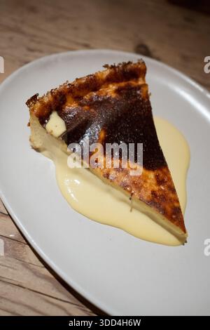 Basque Burnt Cheesecake Scheibe, serviert auf einem weißen Teller mit Vanillesauce Stockfoto