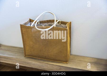 Nahaufnahme der braunen Strandtasche mit Griffen auf Holzoberfläche gegen helle Wand. Griechenland. Stockfoto