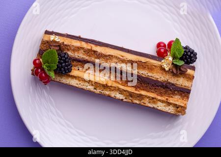 Draufsicht Nahaufnahme der Schokoladenkuchenscheibe mit Beeren - flache Lagenkomposition auf lila Hintergrund. Stockfoto