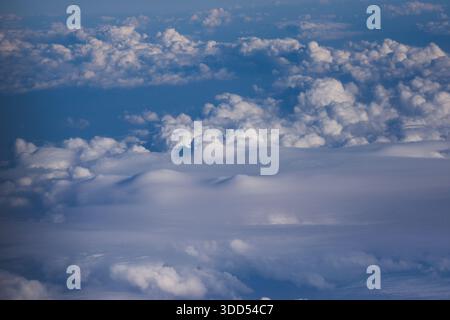 Luftaufnahme einer riesigen Wolkendecke von einem Flugzeugfenster aus. Die Perspektive ist von oben über den Wolkenschichten und blickt hinunter auf dichten, flauschigen Witz Stockfoto